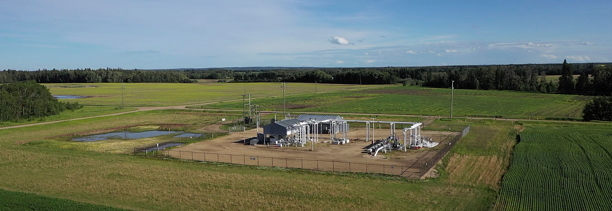 Vue aérienne de la station de pipelines entourée d'herbe, de champs et de zones boisées derrière la station.