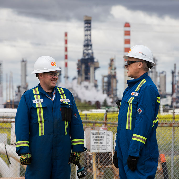 Deux techniciens de pipeline portant leur combinaison bleue et de l’équipement de protection individuelle sur le site d'une installation se parle les uns aux autres.