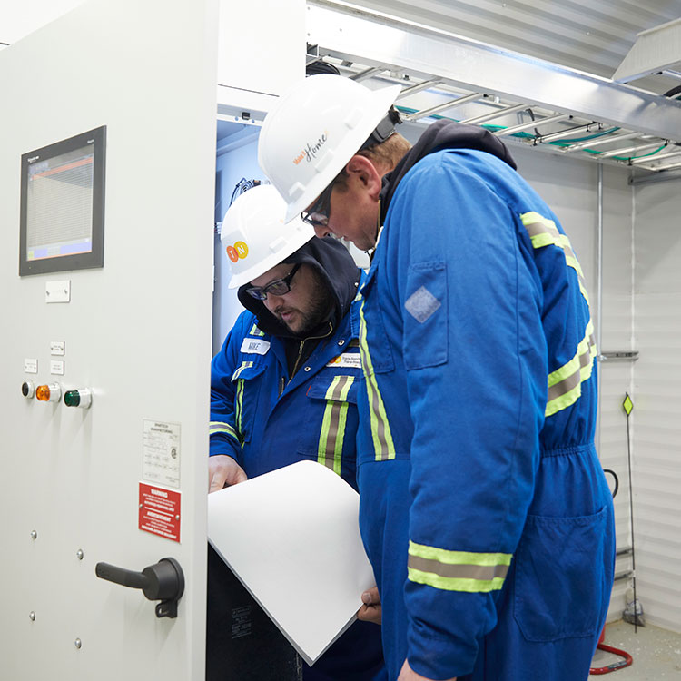 Deux techniciens de pipeline examinent la documentation pour un panneau de commande de station.