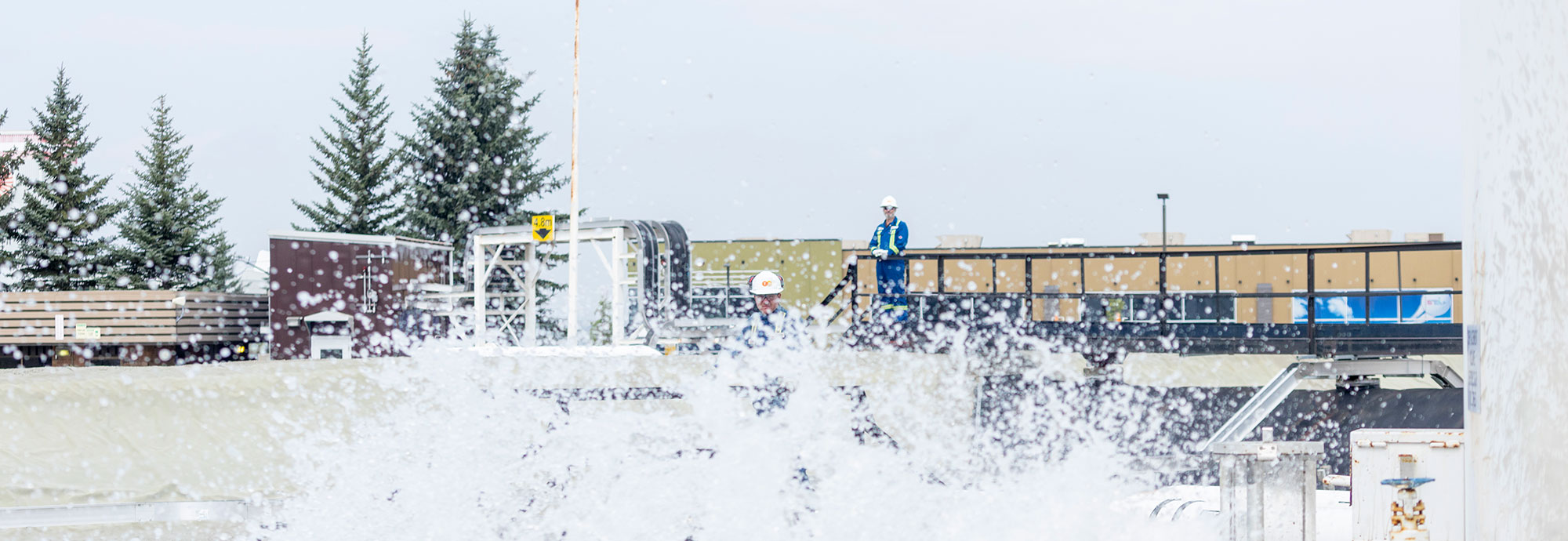 Un technicien de pipeline observe que son collègue déploie de la mousse ignifuge que vous pouvez voir pulvériser vers l'objectif de la caméra.