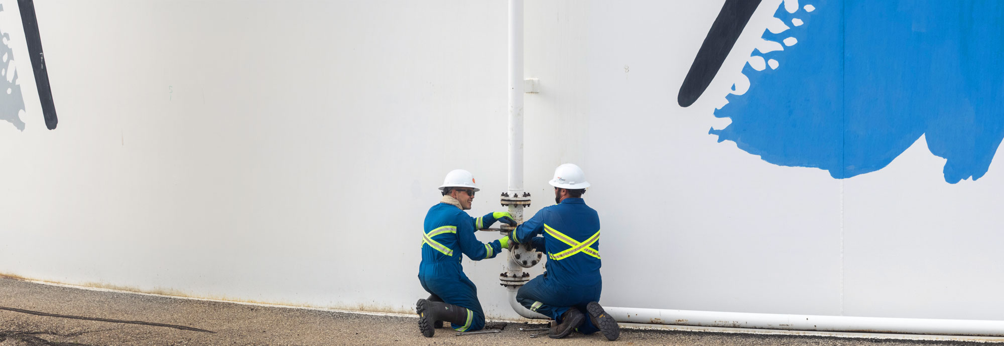 Deux techniciens de pipeline sont agenouillés, ajustant une vanne sur un réservoir de carburant.