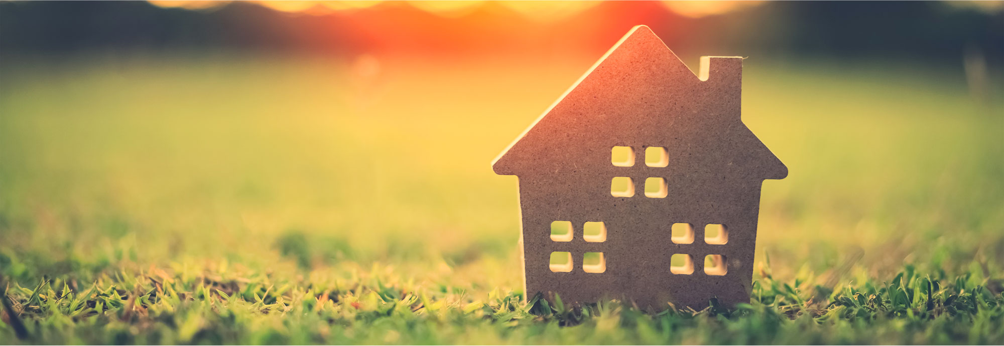 Une découpe d'une petite maison est située sur une pelouse, avec le soleil se levant en arrière-plan.