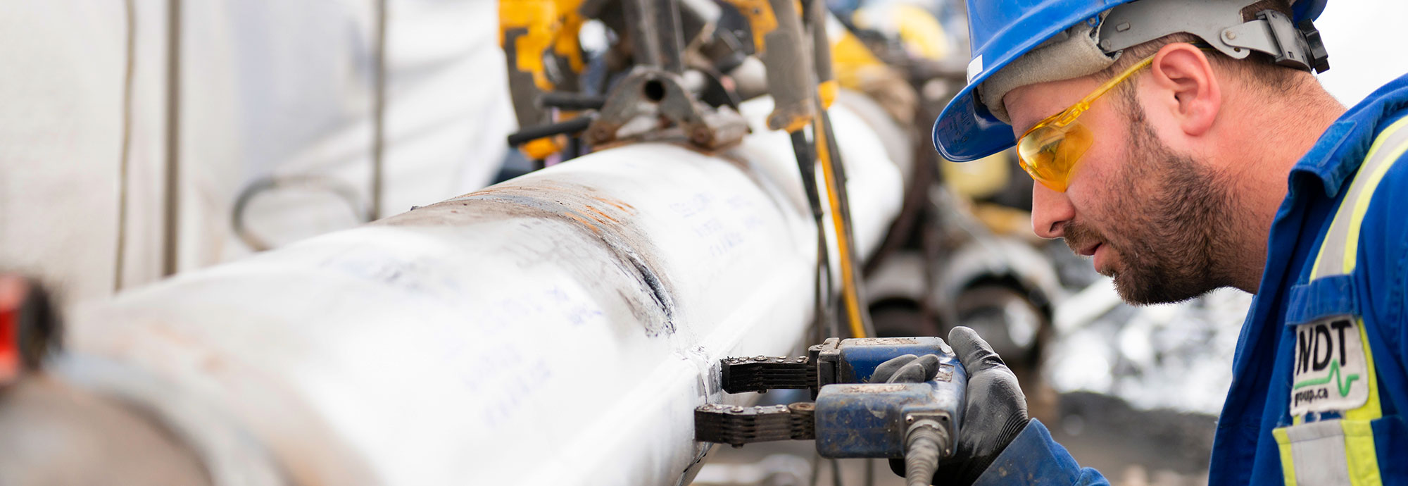 Un technicien de pipeline portant un chapeau de sécurité, des lunettes de sécurité et des gants de travail tient un outil contre un manchon de pipeline.