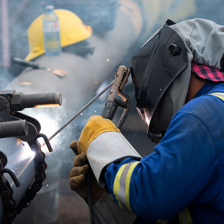 Soudeur travaillant sur une soudure de pipeline, portant son équipement de protection individuelle.