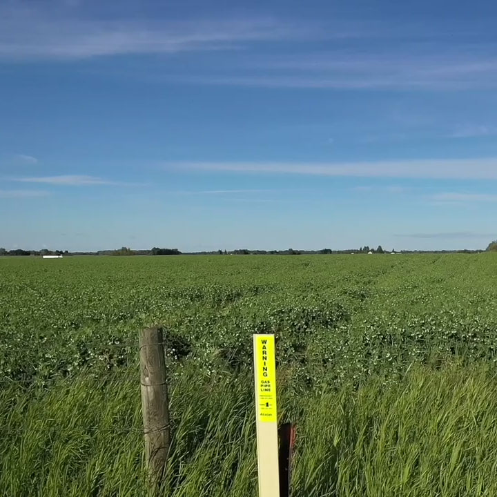 Marqueur de pipeline près d'un poteau de clôture le long d'un terrain agricole.