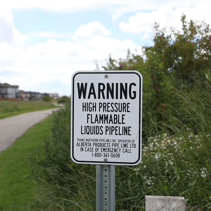 Marqueur blanc de pipeline APPL avec écriture anglaise à côté d'une piste cyclable dans une communauté résidentielle.