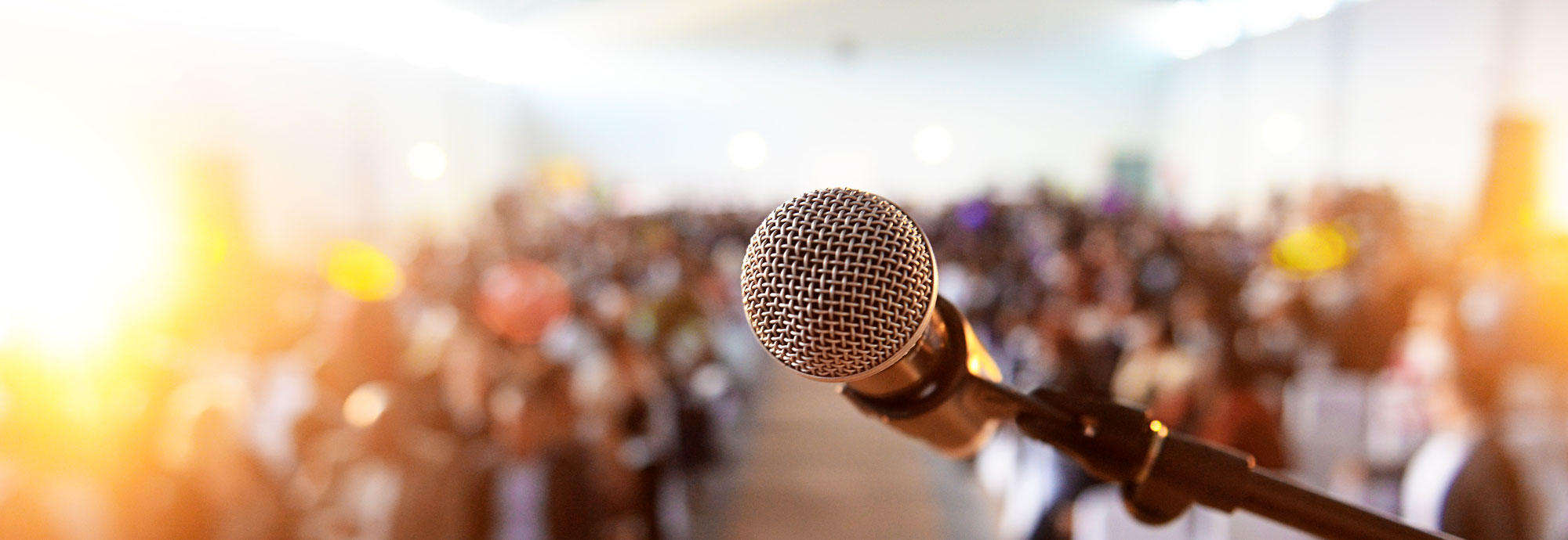 Un microphone est au point, avec une foule floue de personnes assises devant.